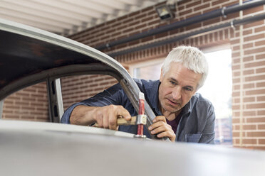 Fokussierter Mechaniker mit Hammer auf der Motorhaube in einer Autowerkstatt - CAIF11213