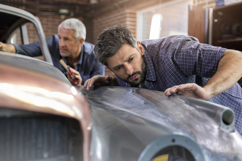 Fokussierter Mechaniker, der in einer Autowerkstatt ein Oldtimer-Panel untersucht, lizenzfreies Stockfoto