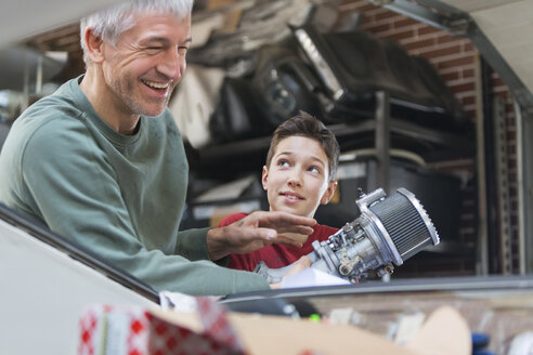 Lächelnder Vater und Sohn reparieren einen Automotor in einer Autowerkstatt - CAIF11241