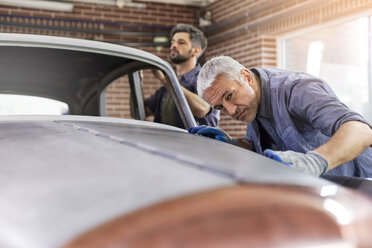 Fokussierter Mechaniker, der in einer Autowerkstatt ein Oldtimer-Panel untersucht - CAIF11244