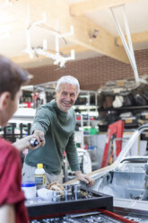 Lächelnder Vater nimmt Werkzeug vom Sohn in der Autowerkstatt - CAIF11246