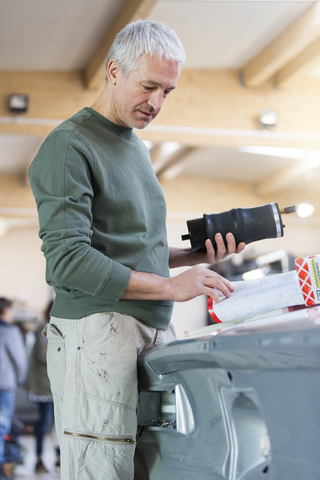 Mechaniker mit Anweisungen zur Überprüfung von Teilen in einer Autowerkstatt, lizenzfreies Stockfoto