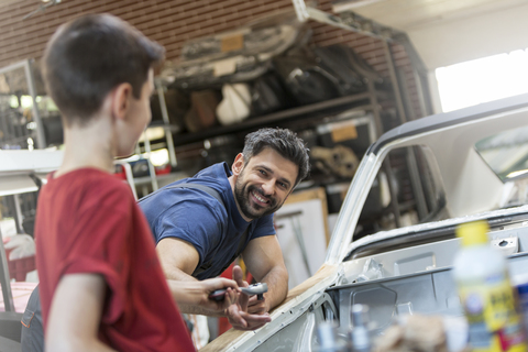 Smiling father taking tool from son in auto repair shop stock photo