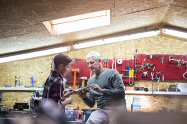 Vater erklärt seinem Sohn in der Autowerkstatt das Werkzeug - CAIF11259