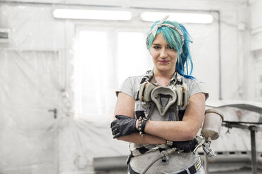 Portrait confident young woman with blue hair with paint gun in auto body shop - CAIF11266