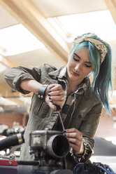 Junge Mechanikerin mit blauen Haaren repariert Automotor in Autowerkstatt - CAIF11270