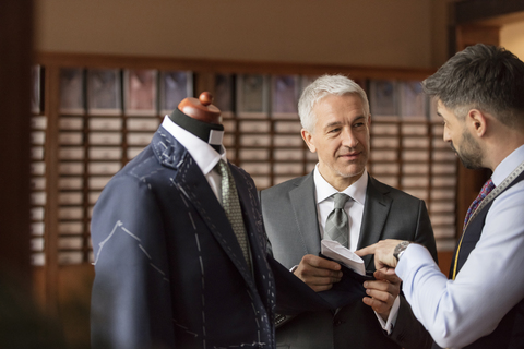 Ein Schneider erklärt einem Geschäftsmann in einem Herrenbekleidungsgeschäft einen Anzug, lizenzfreies Stockfoto