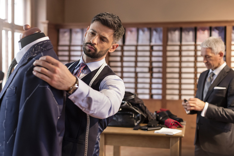 Schneiderin, die einen Anzug an einem Schneidermodell in einem Herrenbekleidungsgeschäft anpasst, lizenzfreies Stockfoto