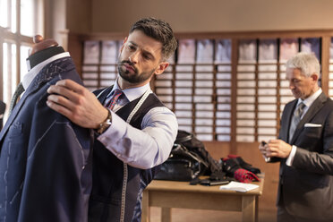 Schneiderin, die einen Anzug an einem Schneidermodell in einem Herrenbekleidungsgeschäft anpasst - CAIF11287