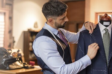 Tailor adjusting suit on dressmakers model in menswear shop - CAIF11296