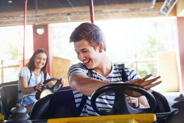 Smiling young man riding bumper cars at amusement park - CAIF11323