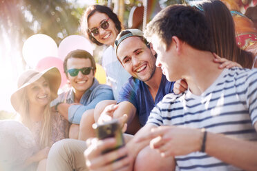 Smiling friends texting with cell phone at amusement park - CAIF11329