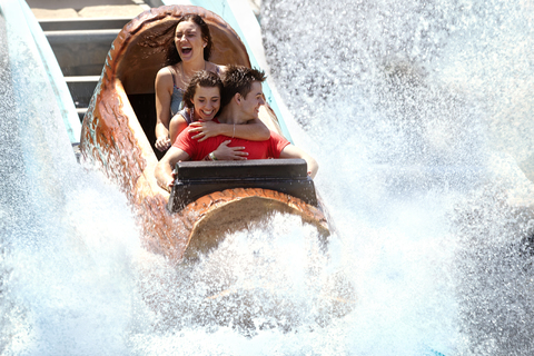 Enthusiastische Freunde, die sich in einer Wasserbahn im Vergnügungspark bespritzen lassen, lizenzfreies Stockfoto