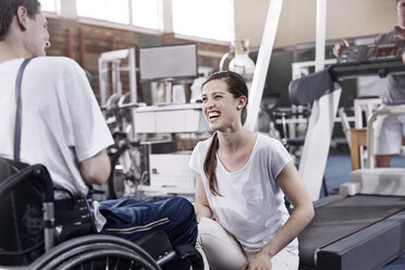 Lächelnde Physiotherapeutin im Gespräch mit Mann im Rollstuhl - CAIF11341