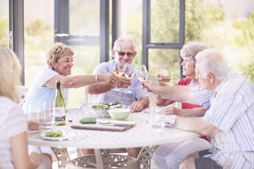 Ältere Erwachsene stoßen beim Mittagessen im Innenhof mit Weingläsern an - CAIF11377