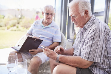 Senior men texting with cell phone on patio - CAIF11378