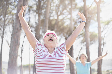 Ältere Frau streckt die Arme in einer Yogastunde in einem sonnigen Park über Kopf - CAIF11379