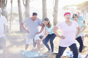 Yoga instructor guiding senior man in sunny park - CAIF11385