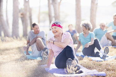 Lächelnde ältere Frau übt Yoga im sonnigen Park - CAIF11392
