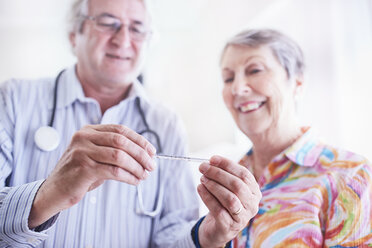 Arzt zeigt einer älteren Frau das Thermometer - CAIF11404