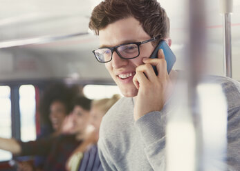 Lächelnder Mann mit Brille, der im Bus mit seinem Handy telefoniert - CAIF11433