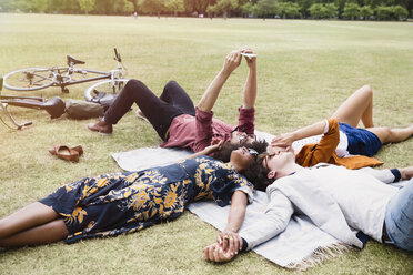 Friends relaxing and taking selfie in circle on blanket in park - CAIF11453