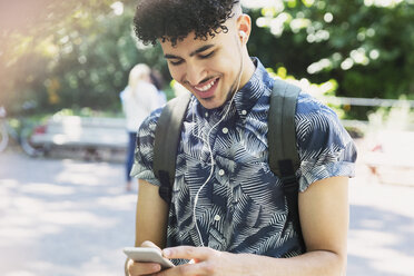 Smiling man with curly black hair listening to music with headphones and mp3 player - CAIF11456