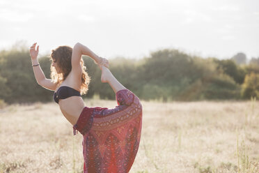 Boho Frau in König Tänzer Yoga-Pose in sonnigen ländlichen Feld - CAIF11477