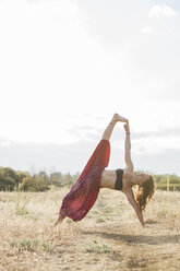 Boho Frau in erweiterten Seite Planke Yoga-Pose in sonnigen ländlichen Feld - CAIF11479