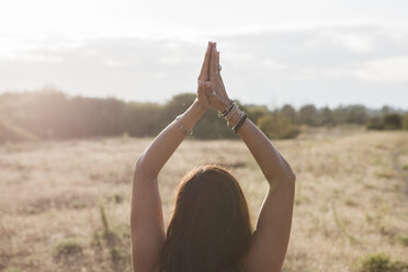 Woman meditating with hands clasped overhead in sunny rural field - CAIF11482