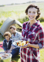 Porträt einer lächelnden Frau mit Gemüsespießen auf einem Campingplatz - CAIF11490