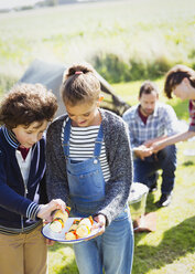 Bruder und Schwester betrachten Gemüsespieße auf einem sonnigen Campingplatz - CAIF11495