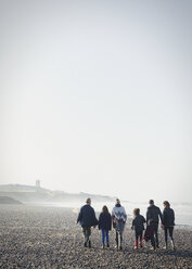 Multi-generation family walking on sunny beach in a row - CAIF11497