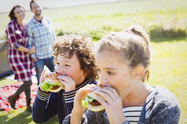 Bruder und Schwester essen Hamburger auf einem sonnigen Campingplatz - CAIF11504