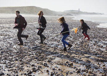 Family running on rocky beach - CAIF11505