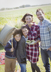 Porträt einer lächelnden Familie mit gegrillten Hamburgern auf einem sonnigen Campingplatz - CAIF11507