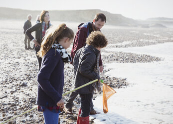 Mehrgenerationen-Familie beim Muschelsammeln am felsigen Strand - CAIF11522