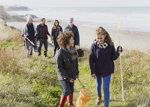 Mehrgenerationenfamilie mit Netzen beim Spaziergang auf dem sonnigen Grasstrandweg, lizenzfreies Stockfoto