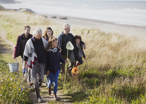 Mehrgenerationen-Familie beim Spaziergang mit Netzen und Eimern auf dem sonnigen Grasstrandweg, lizenzfreies Stockfoto