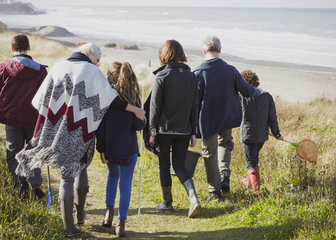 Mehrgenerationenfamilie bei einem Spaziergang auf dem sonnigen Grasstrandweg, lizenzfreies Stockfoto