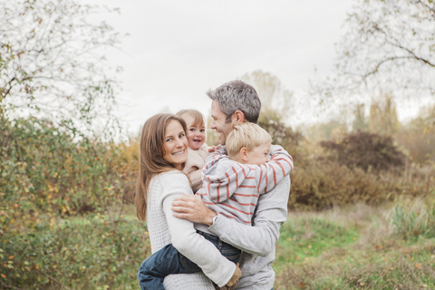 Lächelnde Familie, die sich im Herbst im Park umarmt, lizenzfreies Stockfoto