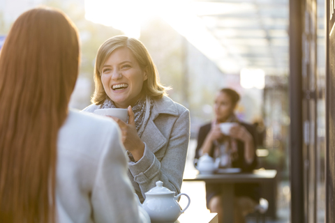 Frauen lachen und trinken Tee in einem Straßencafé, lizenzfreies Stockfoto