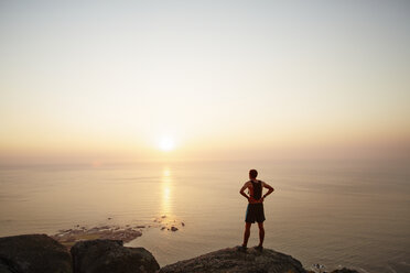 Männlicher Läufer auf Felsen mit Blick auf den Sonnenuntergang am Meer - CAIF11566