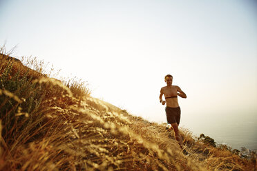 Bare chested man running on sunny hillside - CAIF11570