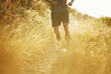 Man running on sunny trail through tall grass - CAIF11572