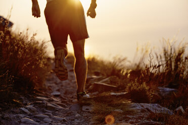 Man running on craggy trail at sunset - CAIF11573