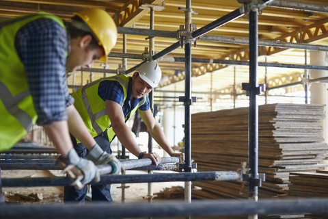 Bauarbeiter beim Einstellen einer Metallstange auf der Baustelle, lizenzfreies Stockfoto