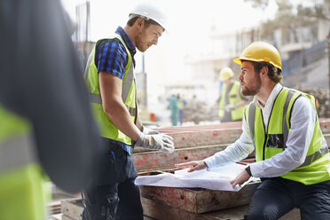 Construction worker and engineer reviewing blueprints at construction site - CAIF11593