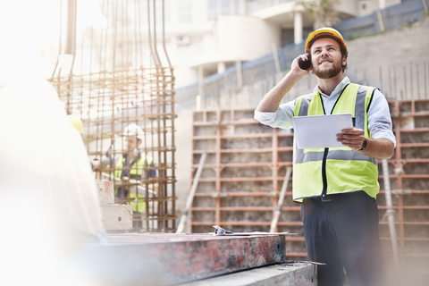 Ingenieur mit digitalem Tablet, der auf einer Baustelle mit einem Handy telefoniert, lizenzfreies Stockfoto