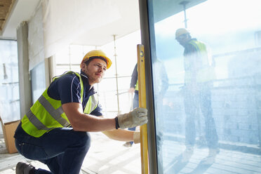 Bauarbeiter mit Nivelliergerät am Fenster auf der Baustelle - CAIF11602